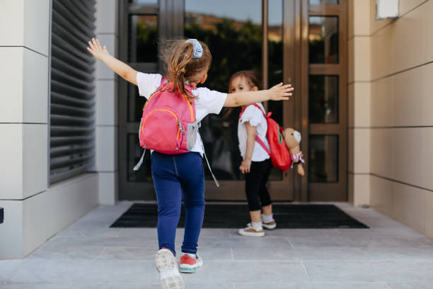 Portrait of smiling little pretty girls holding hands , wearing backpacks and walking to school.